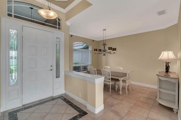 Entryway of a lakefront home in Windermere, featuring a spacious foyer with double doors, tile flooring, and a dining area with a chandelier and white furniture, highlighting elegant interior design.