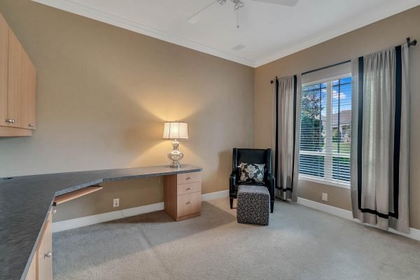Home office space with a desk, lamp, and armchair, featuring large windows with natural light and views of the outdoors, highlighting a comfortable working environment in a Windermere lakefront home.