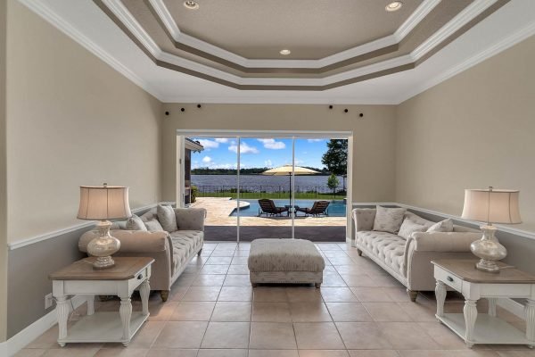 Living room with elegant furnishings and lake views, featuring two sofas, side tables with lamps, and sliding glass doors leading to a pool area in a waterfront home at 2039 Water Key Drive, Windermere, FL.