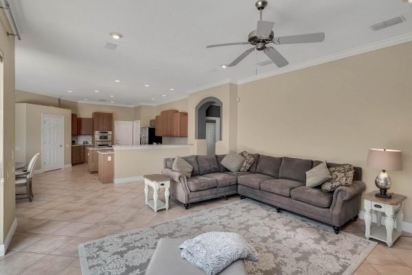 Living room interior of a lakefront home in Windermere, featuring a spacious layout with a sectional sofa, decorative rug, and ceiling fan, showcasing a modern design and open access to the kitchen area.