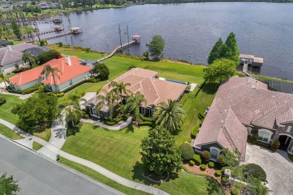 Aerial view of a lakefront home at 2039 Water Key Drive in Windermere, FL, featuring lush landscaping, palm trees, and a serene lake with a dock.