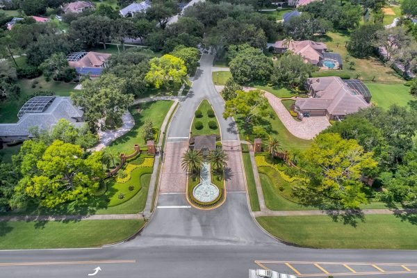 Aerial view of the entrance to a luxury residential community in Windermere, FL, featuring landscaped gardens, palm trees, and a decorative fountain, highlighting the upscale neighborhood atmosphere.