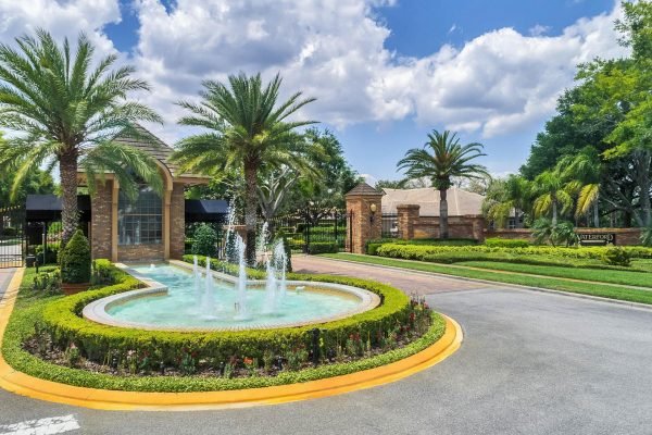 Gated entrance of a luxury community in Windermere, FL, featuring a circular fountain surrounded by lush landscaping and palm trees, indicative of upscale living near Lake Roberts.