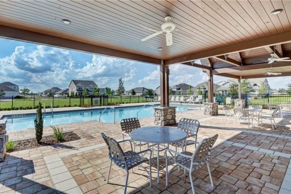 Community pool area with seating and shaded pavilion at The Preserve at Turtle Creek in Saint Cloud, Florida, featuring lush green landscape and clear blue skies.
