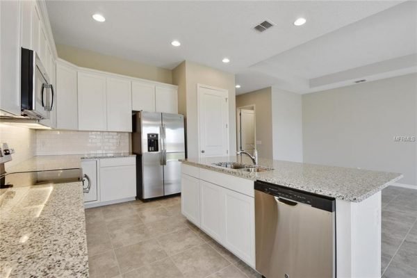 Modern kitchen with granite countertops, stainless steel appliances, and white cabinetry in a new home at 4756 Riverwalk Dr, Saint Cloud, FL, highlighting the spacious layout ideal for family living.