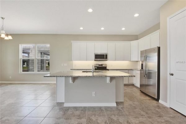Modern kitchen interior featuring stainless steel appliances, granite countertops, and white cabinetry in a new home at 4756 Riverwalk Dr, Saint Cloud, FL.