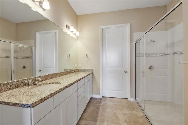 Spacious bathroom featuring dual sinks with granite countertops, large mirror, and walk-in shower, showcasing modern design elements in a new home at 4756 Riverwalk Dr, Saint Cloud, FL.