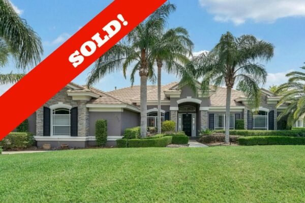 Sold sign overlay on a luxurious lakefront home in Windermere, featuring palm trees, manicured lawn, and elegant architecture.