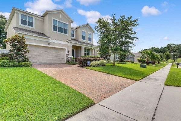 Front view of a two-story single-family home at 2989 Park Meadow Drive, Apopka, FL, featuring a brick paver driveway, manicured lawn, and lush landscaping in a residential neighborhood.