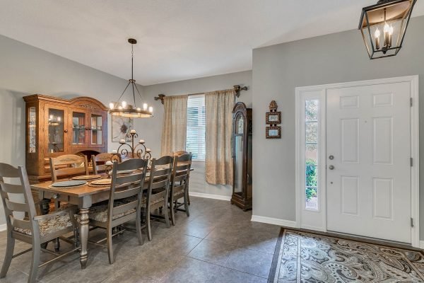 Dining room with wooden table and chairs, chandelier lighting, decorative cabinet, and entrance door, showcasing a welcoming home atmosphere at 2989 Park Meadow Drive, Apopka, FL.