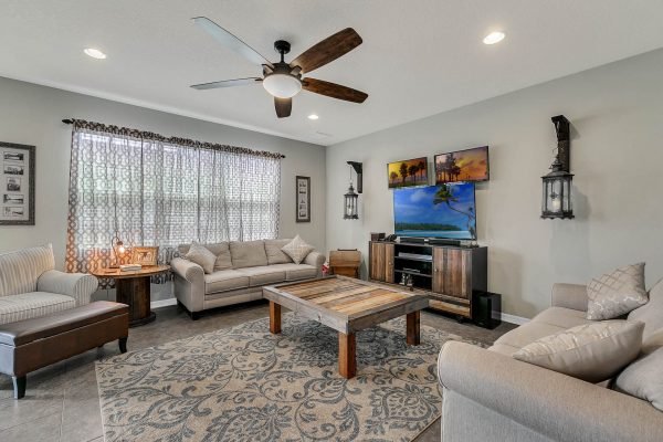 Family room in a home at 2989 Park Meadow Drive, featuring comfortable seating, a wooden coffee table, a television, decorative wall art, and large windows with patterned curtains, highlighting a spacious and inviting atmosphere.