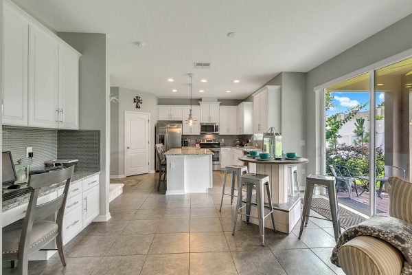 Modern kitchen with white cabinetry, granite countertops, stainless steel appliances, and a breakfast bar, showcasing an open layout and natural light from large windows, ideal for family gatherings in a home at 2989 Park Meadow Drive, Apopka, FL.
