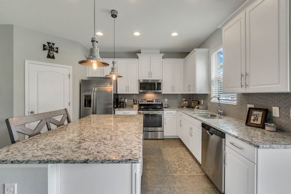 Modern kitchen with granite countertops, stainless steel appliances, and white cabinetry, featuring a spacious island and pendant lighting, ideal for gatherings and meal prep.