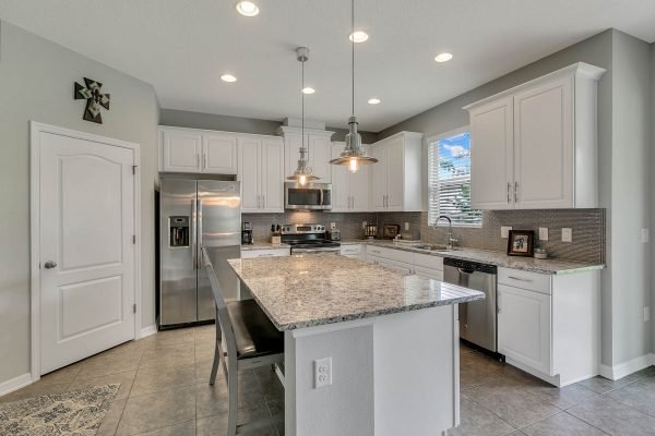 Modern kitchen with granite countertops, stainless steel appliances, white cabinetry, and an island, featuring pendant lighting and a spacious layout, located in a home at 2989 Park Meadow Drive, Apopka, FL.