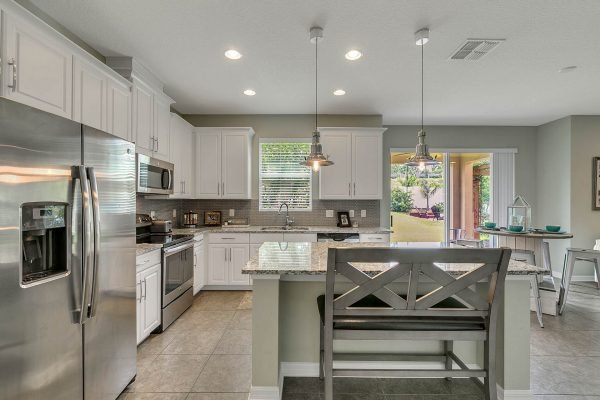 Modern kitchen in Apopka, FL, featuring stainless steel appliances, granite countertops, white cabinetry, and an open layout with a breakfast bar and natural light.