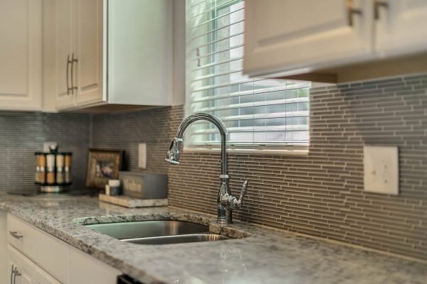 Modern kitchen with granite countertops, stainless steel sink, and stylish faucet, featuring light cabinetry and a mosaic backsplash, ideal for the home at 2989 Park Meadow Drive, Apopka, FL.