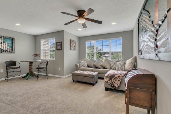 Spacious living room in a single-family home at 2989 Park Meadow Drive, featuring a cozy sectional sofa, decorative pillows, a ceiling fan, and natural light from large windows, complemented by a small dining area with bar stools.