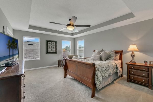 Master bedroom featuring a king-size bed, decorative pillows, and a stylish ceiling fan, with large windows providing natural light, a wooden dresser, and a cozy atmosphere, showcasing the spacious layout of 2989 Park Meadow Drive, Apopka, FL.