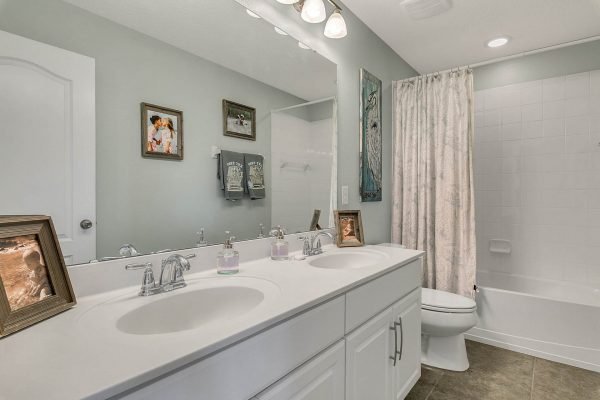 Modern bathroom with double sinks, framed artwork, and a shower-tub combo, showcasing clean lines and neutral colors, ideal for the listing at 2989 Park Meadow Drive, Apopka, FL.