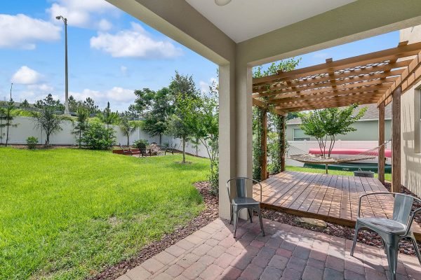 Backyard view of 2989 Park Meadow Drive, Apopka, FL, featuring a wooden pergola, patio area with chairs, and lush green lawn surrounded by trees and a privacy fence.