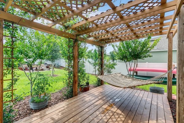 Backyard view of a wooden pergola with a hammock, surrounded by greenery and potted plants, showcasing a private outdoor space at 2989 Park Meadow Drive, Apopka, FL.