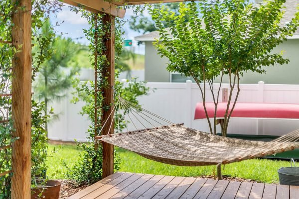 Backyard view of a hammock under a pergola, surrounded by green plants and a privacy fence, showcasing a tranquil outdoor space at 2989 Park Meadow Drive, Apopka, FL.
