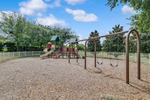Playground with swings and slide set in a fenced area surrounded by trees, located near Magnolia Park Estates in Apopka, FL.
