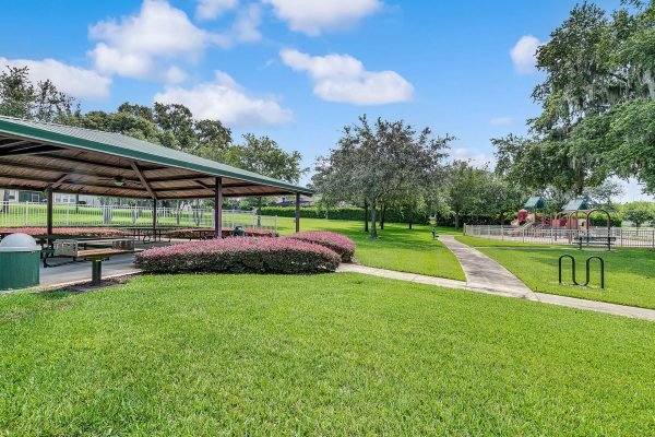 Community park featuring a covered pavilion, manicured lawns, walking paths, and playground equipment in a residential area near Magnolia Park Estates, Apopka, FL.