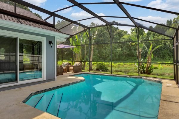 Screened pool area with a private pond view, surrounded by lush greenery, featuring outdoor seating and energy-efficient home elements.