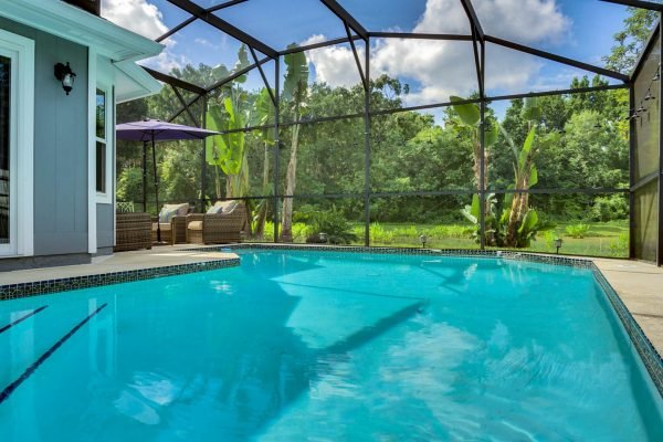 Screened pool with clear blue water, surrounded by lush greenery and conservation area, featuring patio seating and a sunny sky, highlighting the privacy and tranquility of 633 Remington Oak Dr, Lake Mary, FL.