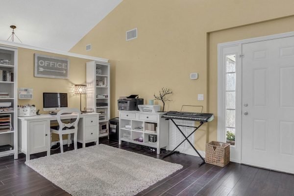 Home office space with white desk, chair, and shelving, featuring a computer and keyboard, located in a bright room with yellow walls, showcasing a welcoming entrance and modern decor.