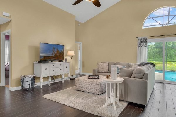 Cozy family room in Lake Mary, FL, featuring a comfortable gray sectional sofa, decorative accent table, and large windows with views of a screened pool and conservation area, ideal for relaxation and privacy.