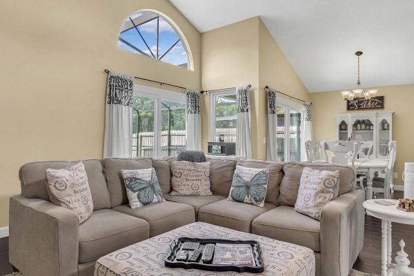 Cozy family room featuring a large sectional sofa with decorative pillows, bright natural light from large windows, and a dining area in the background, ideal for showcasing the inviting atmosphere of 633 Remington Oak Dr, Lake Mary, FL.