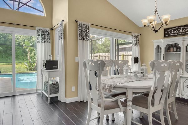 Bright dining area featuring a white table and chairs, large windows with views of a screened pool, and elegant decor, highlighting the serene ambiance of 633 Remington Oak Dr, Lake Mary, FL.