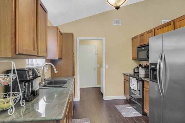 Modern kitchen with wooden cabinets, stainless steel appliances, and a view of the adjoining room, showcasing a clean and inviting space ideal for family gatherings in the Lake Mary home at 633 Remington Oak Dr.