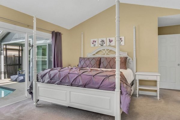 Master bedroom with a four-poster bed, purple bedding, and large windows leading to a screened pool area, showcasing a serene and private atmosphere in a home located at 633 Remington Oak Dr, Lake Mary, FL.