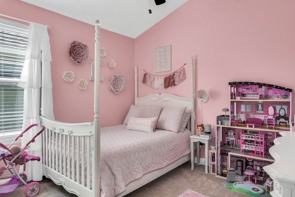Pink-themed bedroom featuring a white crib, decorative wall flowers, and a dollhouse, ideal for a child's room in a family-friendly home.