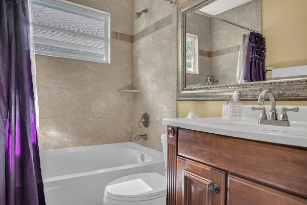 Bathroom with a bathtub, brown wooden vanity, large mirror, and purple curtains, featuring natural light from a window, showcasing a clean and modern design.