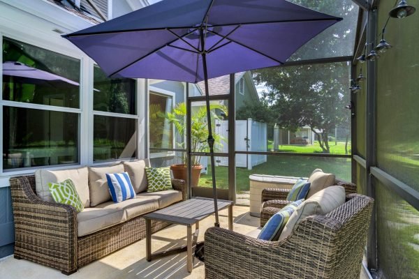 Screened lanai with comfortable seating, umbrella, and views of a lush backyard at 633 Remington Oak Dr, Lake Mary, FL, highlighting private outdoor living space.