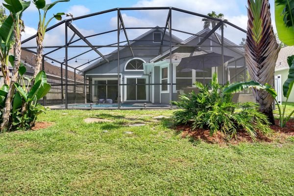 Backyard view of 633 Remington Oak Dr, Lake Mary, FL, featuring a screened pool area surrounded by lush greenery, with a conservation area visible beyond the property, emphasizing privacy and tranquility.