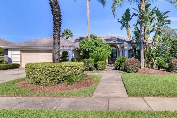 Spacious 3-bedroom remodeled home at 7977 Canyon Lake Cir, Orlando, surrounded by lush landscaping, palm trees, and a well-maintained pathway leading to the entrance.