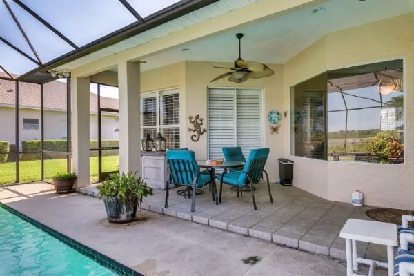Patio area with poolside seating, featuring a table and chairs, surrounded by lush greenery and views of Steer Lake, highlighting the outdoor living space of the 7977 Canyon Lake Cir property in Orlando, FL.
