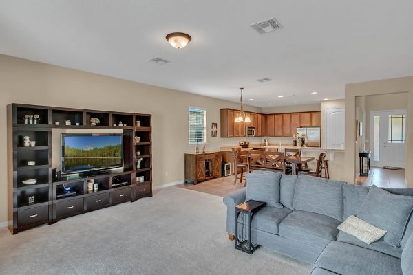Living room with gray sectional sofa, TV unit, and open kitchen in Windermere home, showcasing spacious layout and modern design features.
