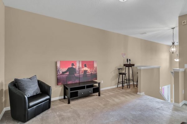 Loft area in Windermere home featuring a black armchair, entertainment unit with artwork, and bar stools against a beige wall, showcasing a spacious and inviting design.