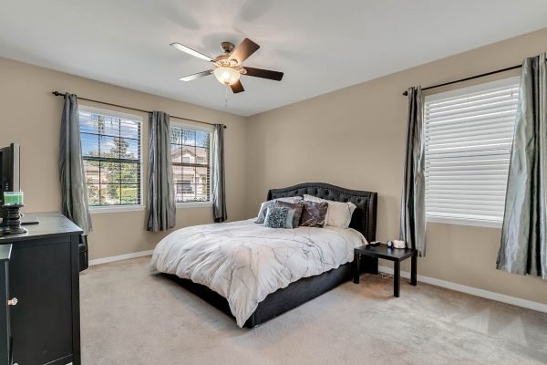 Master bedroom in Windermere home featuring a queen-sized bed, two windows with curtains, a ceiling fan, and a nightstand, showcasing spacious layout and natural light.