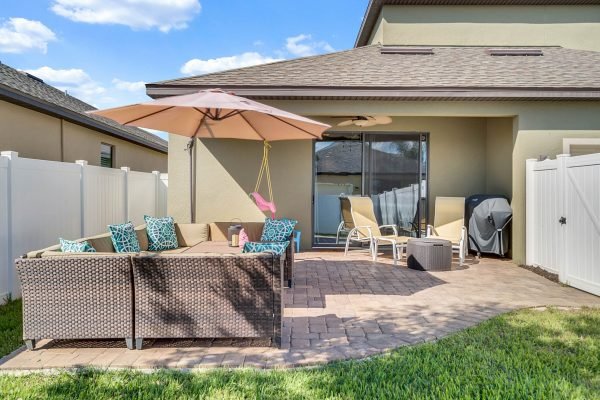 Patio area of a meticulously cared for Windermere home featuring a covered lanai, outdoor seating with colorful cushions, and a large umbrella, surrounded by a fully fenced yard and paver patio, ideal for enjoying Florida weather.