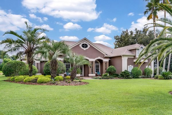 Custom home at 17744 Deer Isle Cir in Winter Garden, FL, featuring lush tropical landscaping, palm trees, manicured lawns, and a welcoming front entry with double doors, set on a spacious acre lot in the exclusive Deer Island community.