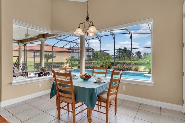 Dining area with a table set for breakfast, featuring a view of the screened-in pool and tropical landscaping in the backyard, highlighting the spacious, light-filled interior of the home at 17744 Deer Isle Cir, Winter Garden, FL.