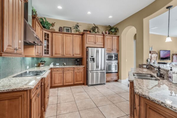 Luxurious kitchen with wooden cabinetry, granite countertops, stainless steel appliances, and tile flooring, showcasing a spacious layout ideal for a lakefront property at 1837 Lake Roberts Landing Dr, Winter Garden, FL.