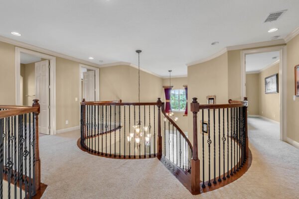 Spacious upstairs landing with elegant curved staircase, decorative railings, and natural light from nearby windows in a luxurious lakefront home at 1837 Lake Roberts Landing Dr, Winter Garden, FL.
